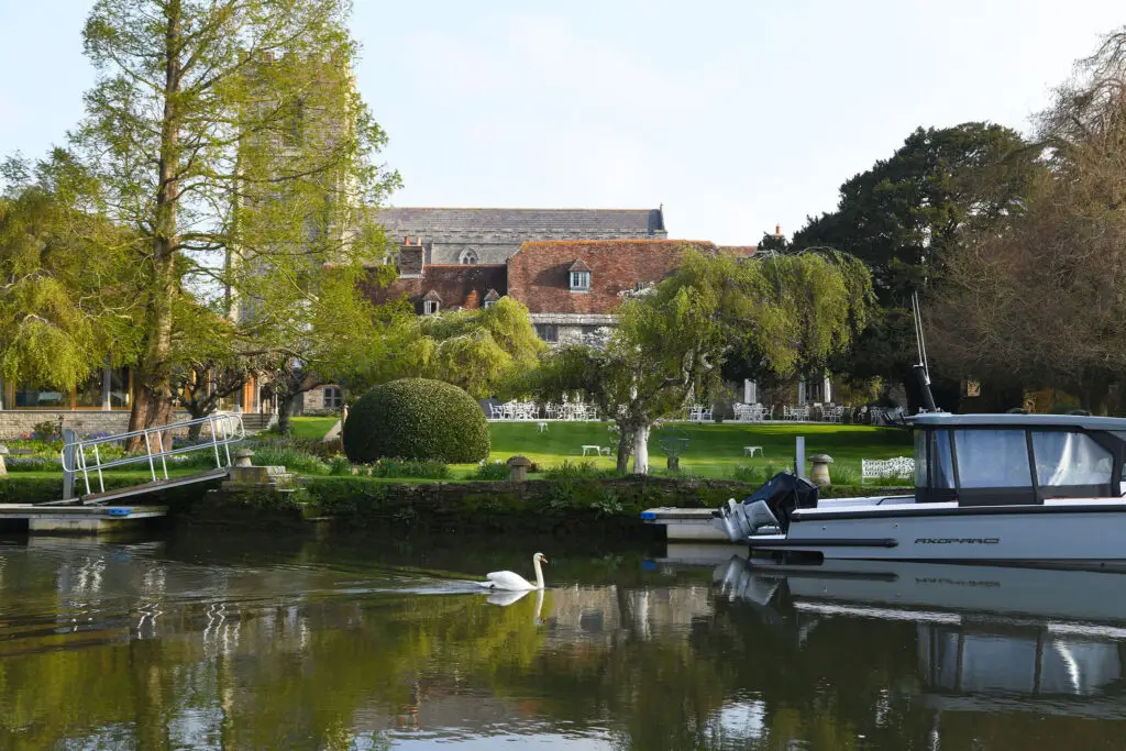 coutnry house hotel on river with green lawna nd boat and swan.
