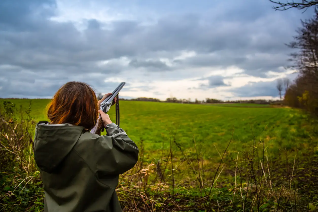 Girl with shotgun shooting on a field in the sunset