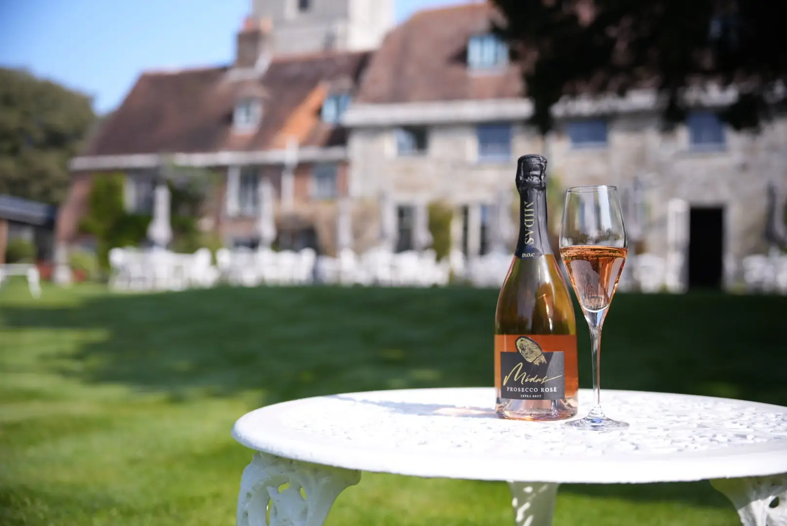 Prosecco bottle and glass of prosecco on white table on a green lawn